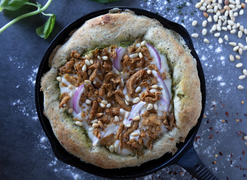 Rotisserie Chicken Pesto Pizza in a cast iron skillet garnished with basil, pine nuts and crushed red pepper