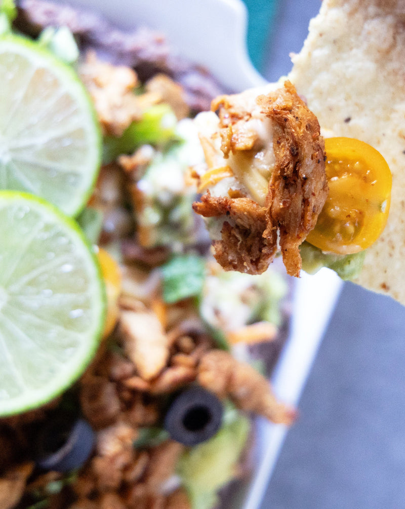 Barvecue Carnitas 7-Layer Dip garnished with limes and tortilla chips